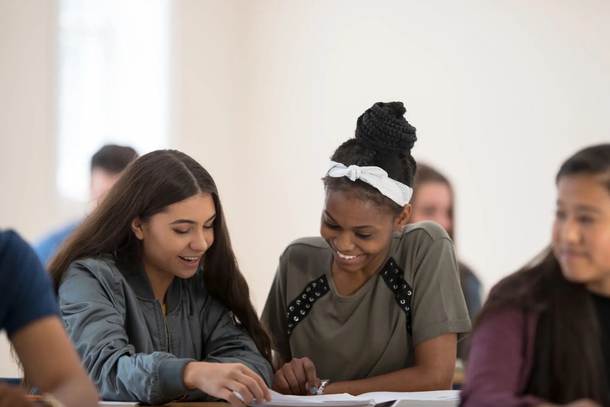 Two young women smiling and working together at a table.